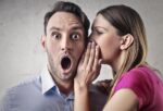 woman whispering something to a shocked man