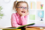 little girl wearing eyeglasses smiling with her bunch of books