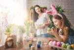 mother and daughter wearing bunny ears painting easter eggs