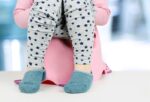 child wearing navy socks, stary grey pajama and pink sweater sitting in pink potty