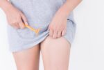 woman in grey shirt about to shave her crotch with a yellow razor