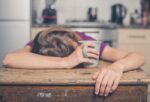 woman sleeping in a wooden table while holding her cup of drink