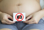 Pregnant woman showing tummy holding a no photo symbol with two hands