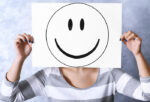 Woman holding a smiley face drawn on a white paper covering her face