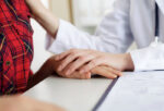 Doctor consoling a woman in red checkers touching her hand and shoulder