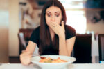 woman eating and feeling sick with hand over her mouth